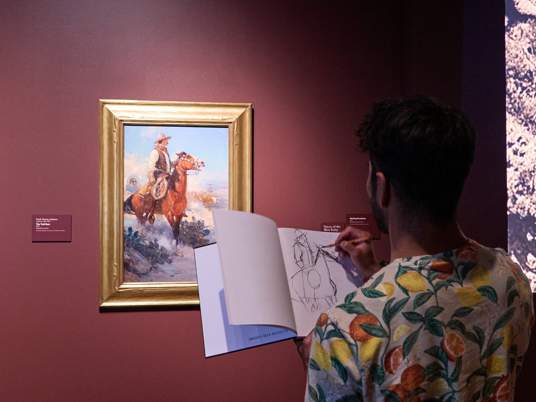 Eine Person steht mit dem Rücken zum Betrachter vor einem Bild in einem Museum und zeichnet dieses in einem Heft nach.