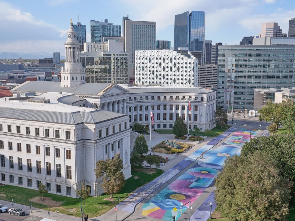 Ein halbrundes, weißes, klassizistisches Gebäude mit einem zentralen Turm: das City and County Building in Denver. Die gesamte Straße davor ist bunt bemalt.