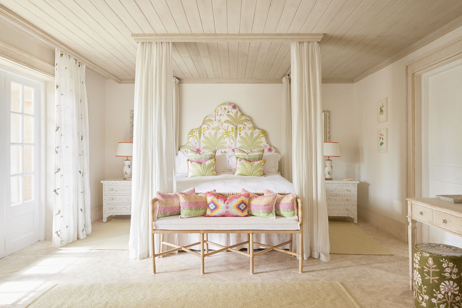Schlafzimmer mit cremefarbenem Himmelbett, blumig gemustertem Kopfteil und farbigen Ikat-Kissen.