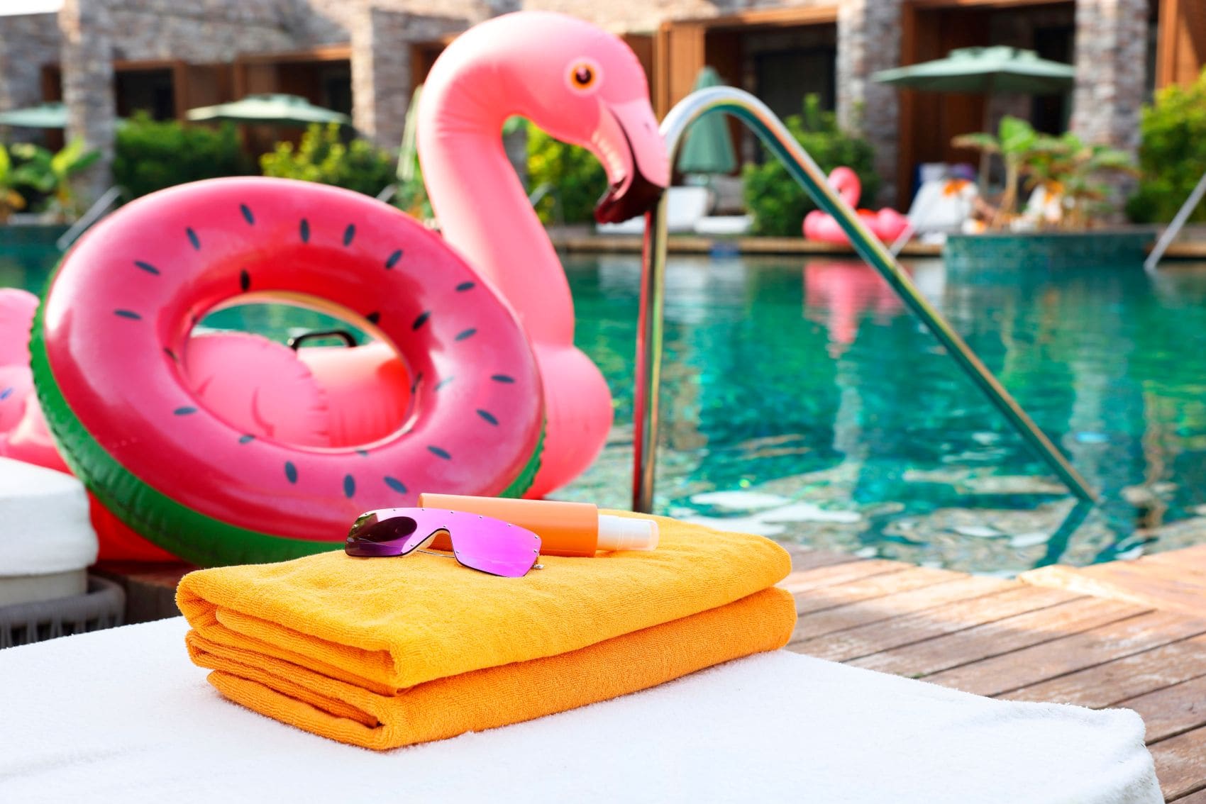 Hotelpool mit Nahaufnahme einer Liege, auf der Handtücher, Sonnenbrille und Sonnencreme liegen 