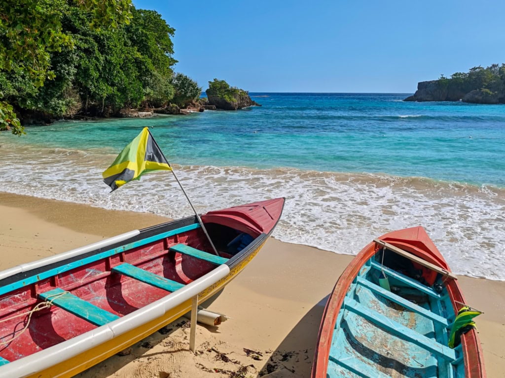 Zwei Boote liegen an einem karibischen Sandstrand; in einem der Boote steckt eine Jamaika-Flagge.