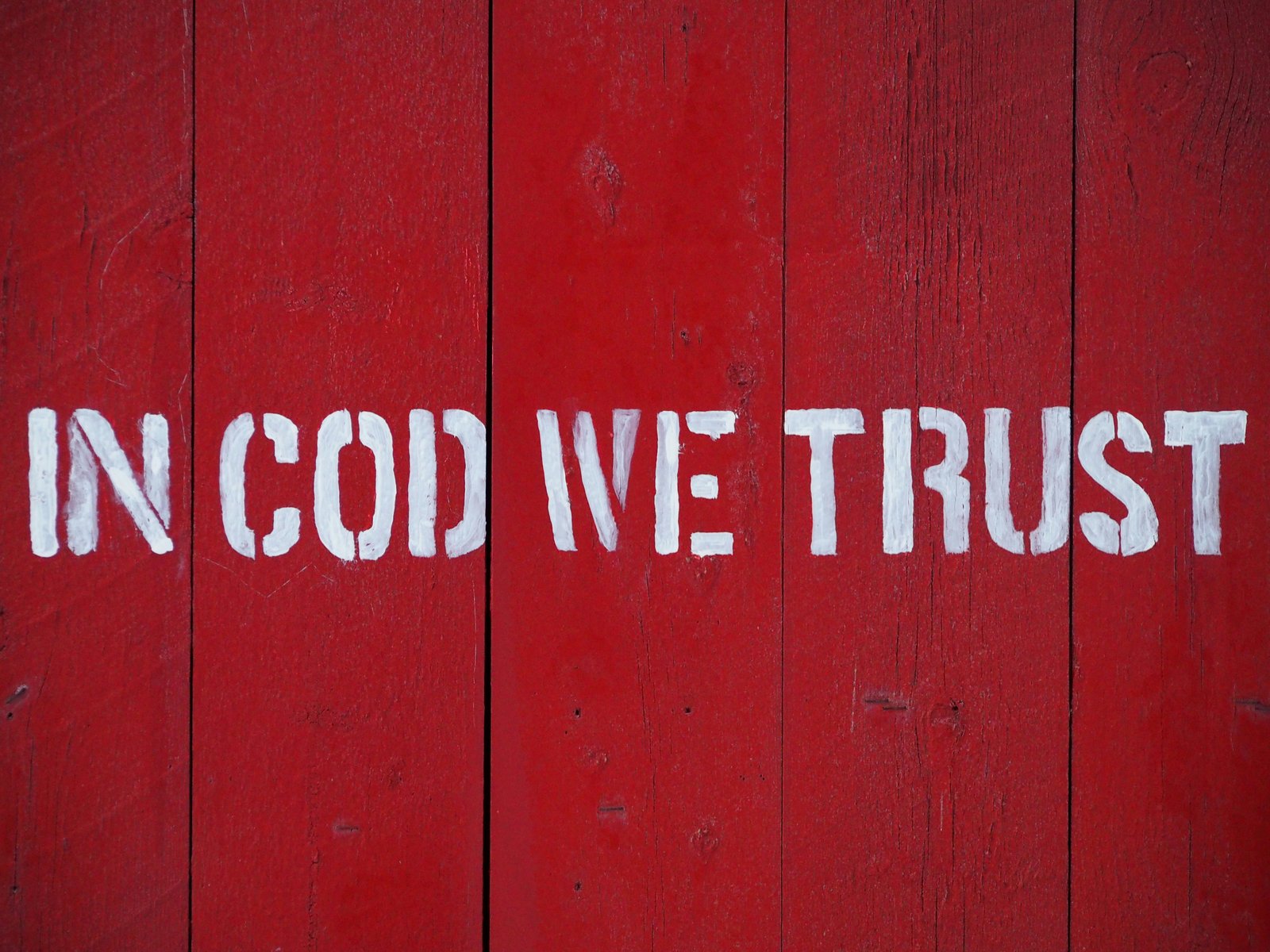 Schriftzug In Cod We Trust in weißer Schablonenfarbe auf der roten Holzwand einer Lofoten-Fischerhütte