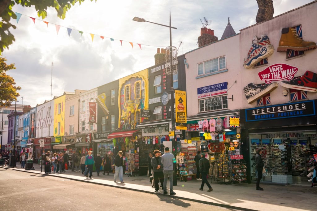 Mehrere Flachdachhäuser, jedes mit bunten, kunstvollen Murals bemalt, stehen dicht an dicht im Sommerlicht in Camden in London.