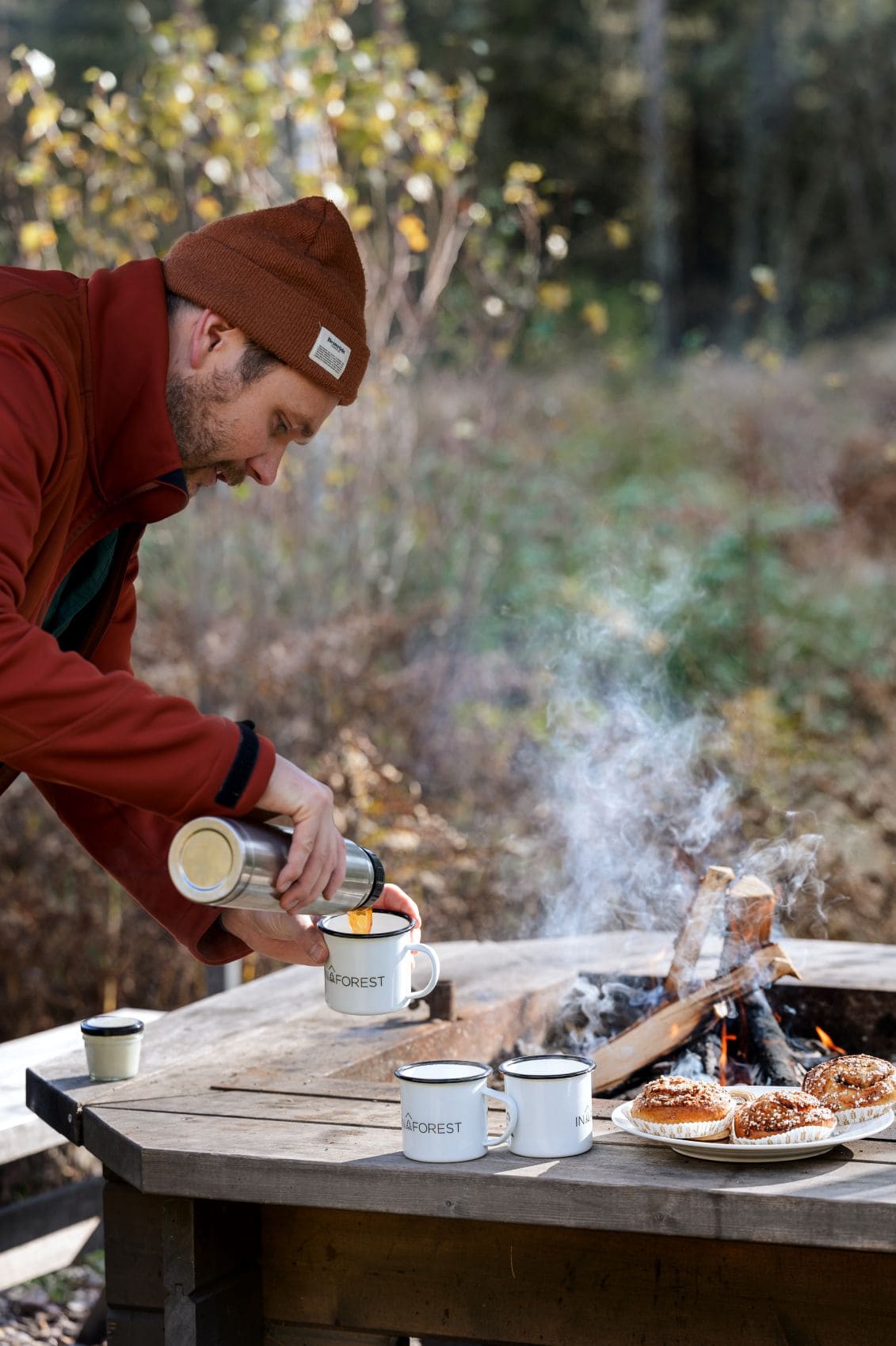 Mann schenkt Kaffee an einer Feuerstelle im Wald in Westschweden ein – naturnahes Outdoor-Erlebnis mit Lagerfeuer und schwedischem Gebäck.