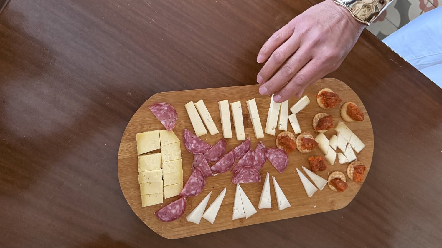 Holzbrett mit menorquinischer Tapas-Auswahl: Würfel und Dreiecke Queso Mahón, Salami-Scheiben und mit Sobrassada belegte Cracker