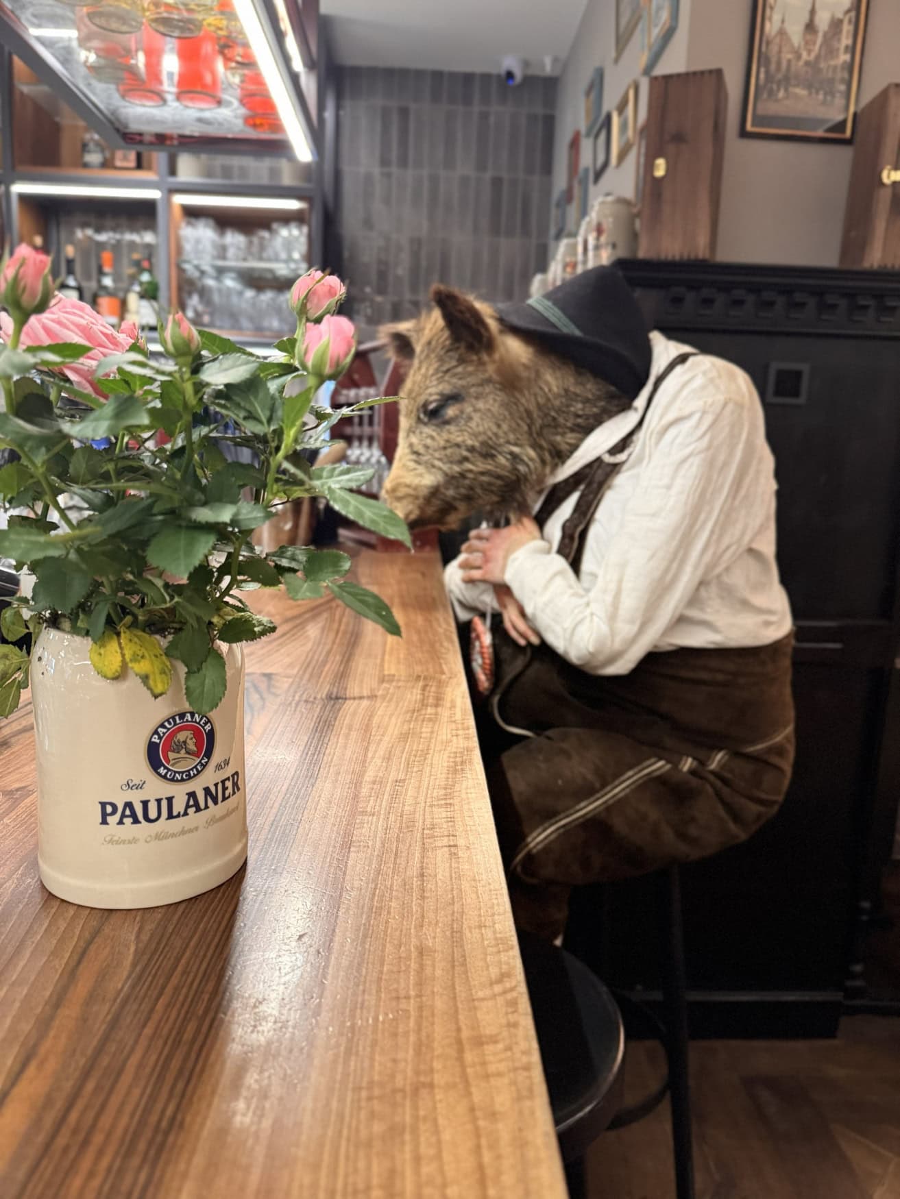 An der Theke eines modernen Brauhauses sitzt eine Puppe in bayerischer Tracht, die einen Wildschweinkopf trägt