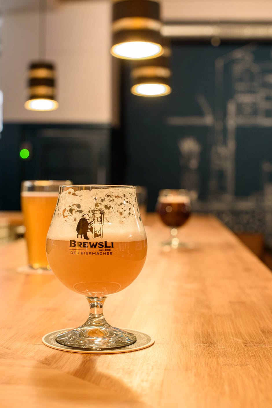 Nahaufnahme eines Biers in einem bauchigen Stielglas auf einem Tresen. Auf dem Glas prangt die Aufschrift "BrewsLi"
