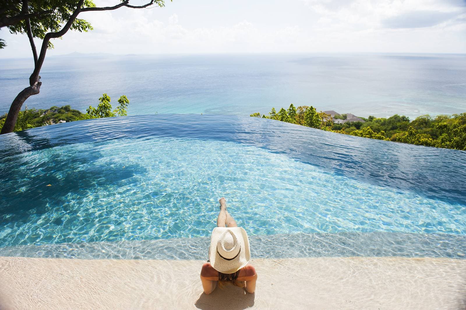 Frau mit Strohhut entspannt am Rand eines Infinity-Pools mit weitem Blick auf das offene Meer.