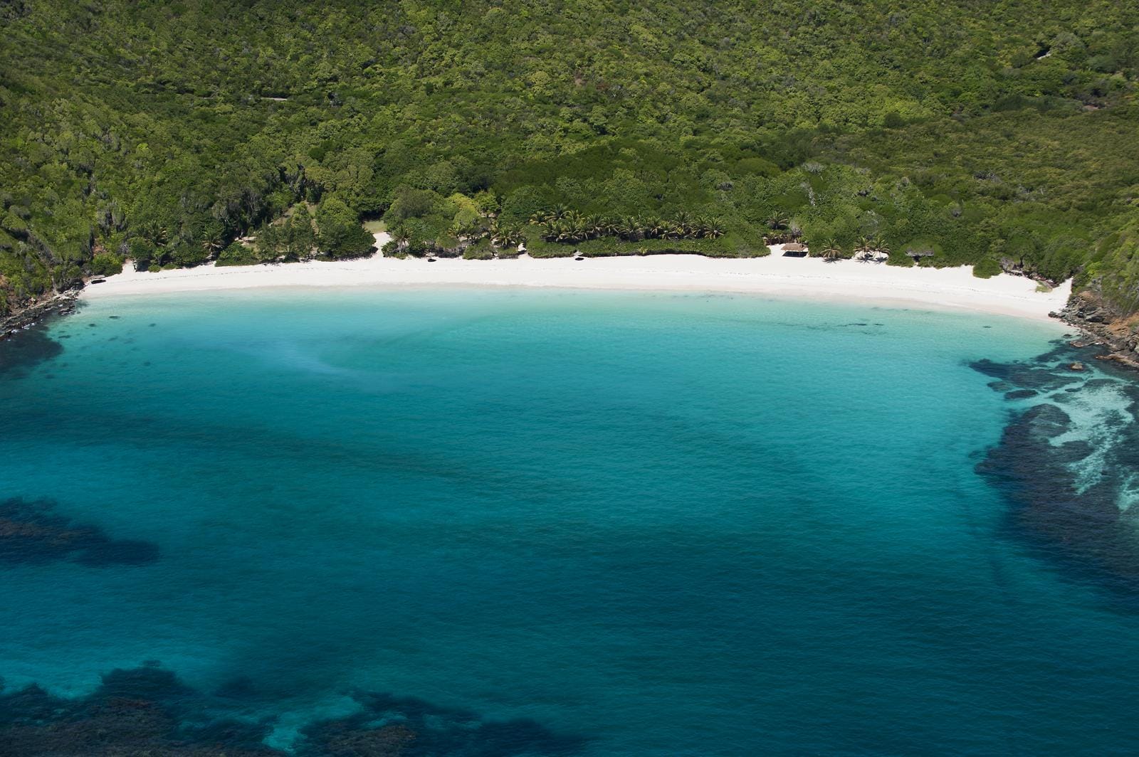 Luftaufnahme einer einsamen Strandbucht von Mustique mit weißem Sand und tiefblauem Wasser.