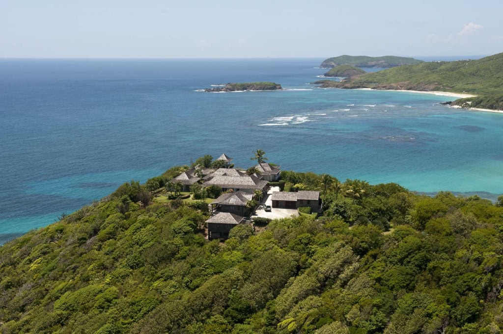 Luftaufnahme der Küste von Mustique mit Villen, dichter Vegetation und vorgelagertem Korallenriff.