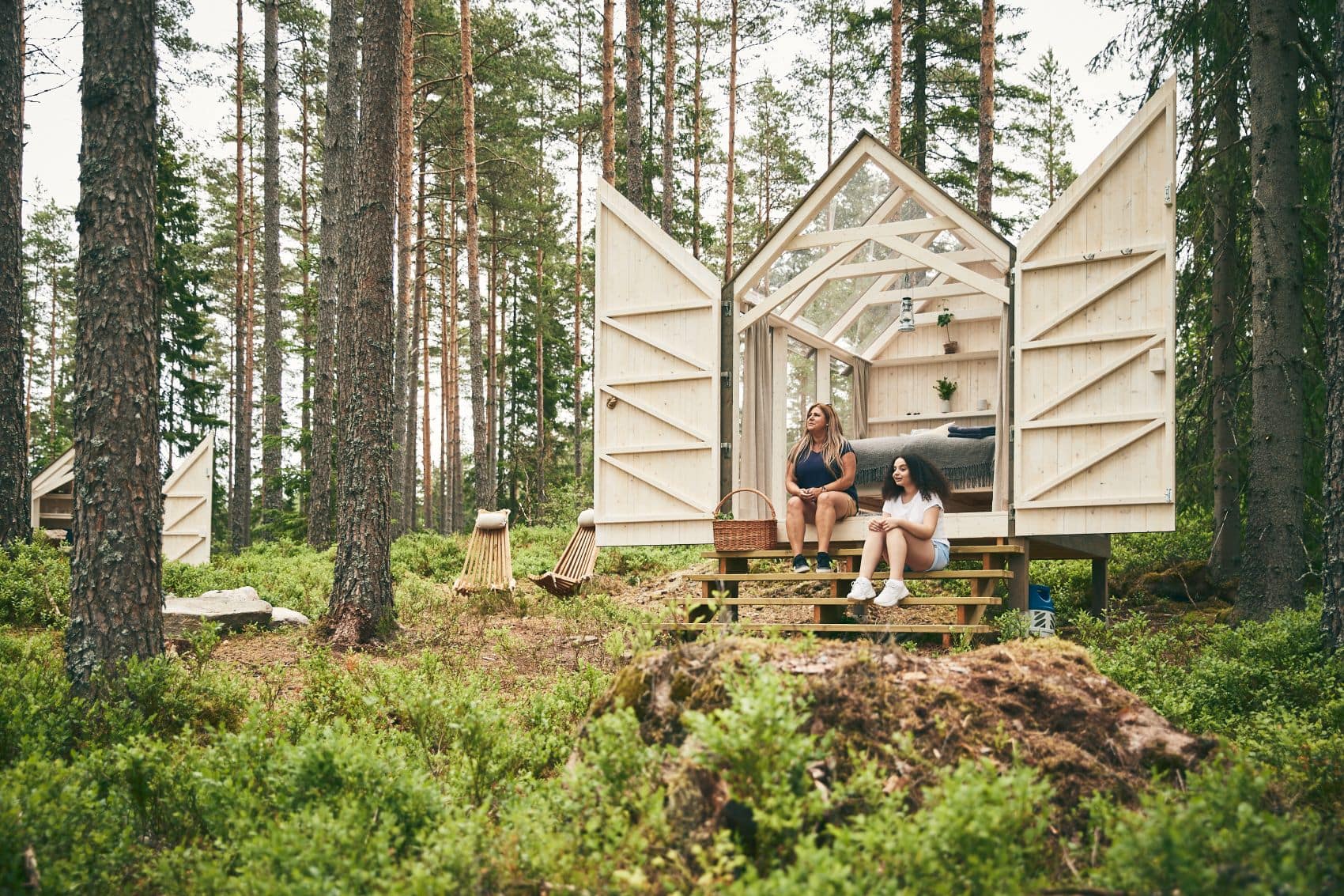 Zwei Frauen sitzen vor ihrem Off-Grid-Cottage in einem Wald in Westschweden 