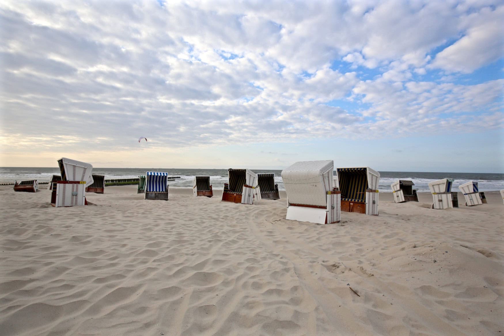 Mehrere weiße Strandkörbe stehen verteilt auf einem weiten Strand.