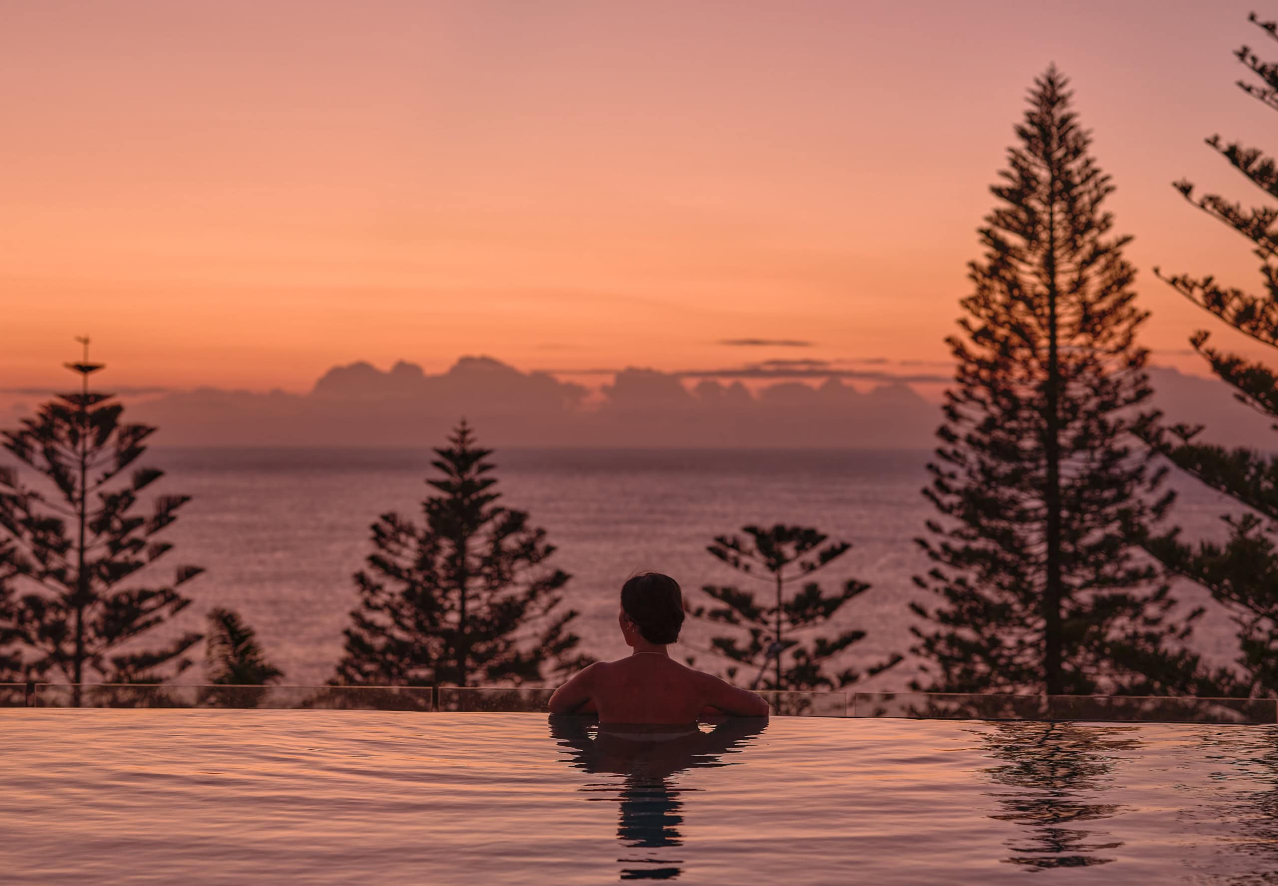 Eine Frau schwimmt im Pool bei Sonnenuntergang.
