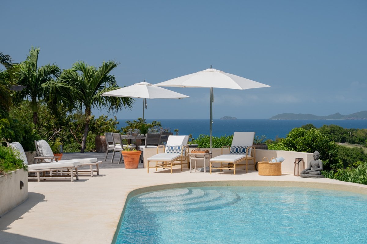 Pool mit Sonnenliegen unter weißen Sonnenschirmen und Blick auf das Meer mit vorgelagerten Inseln.