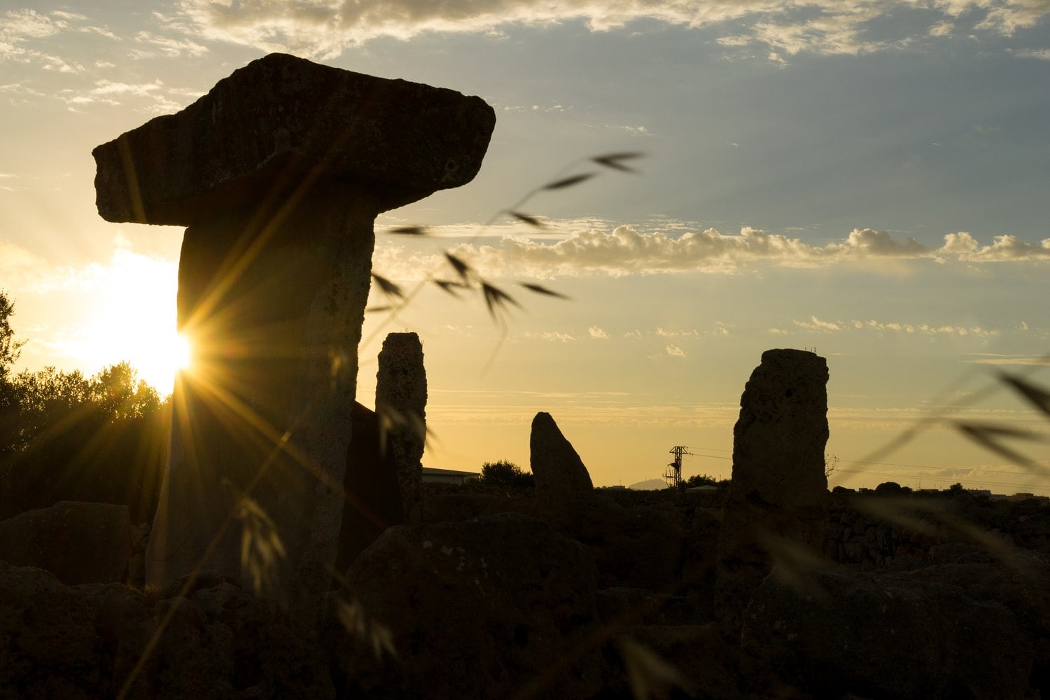 Silhouette einer prähistorischen Talayot-Anlage mit T-förmigem Trilithon und Menhiren gegen die untergehende Sonne, Menorca.