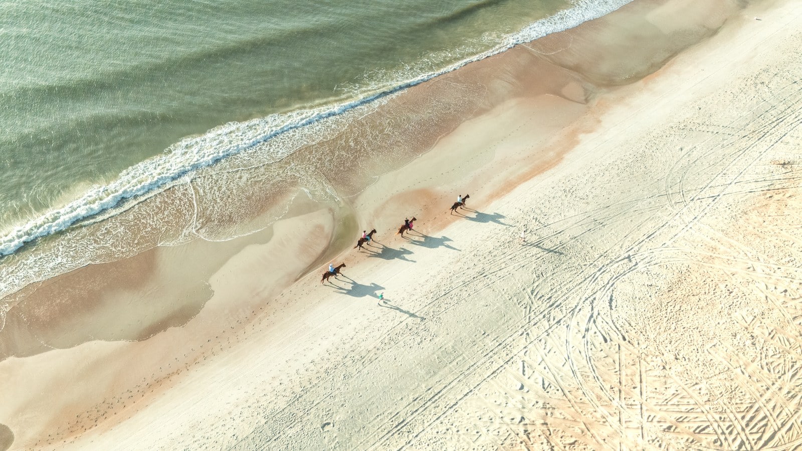 Luftaufnahme von vier Reitern zu Pferd am breiten Sandstrand von Amelia Island entlang der türkisen Brandung
