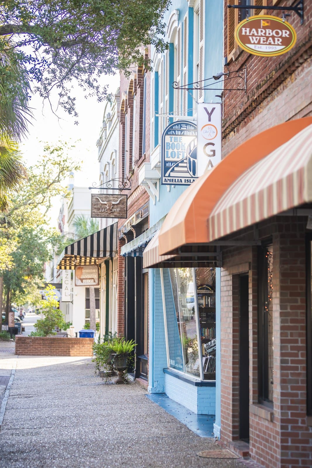 Historische Geschäftsstraße in der Innenstadt von Amelia Island mit bunten Ladenfassaden, Markisen und Schildern wie „Harbor Wear" und „Yoga"