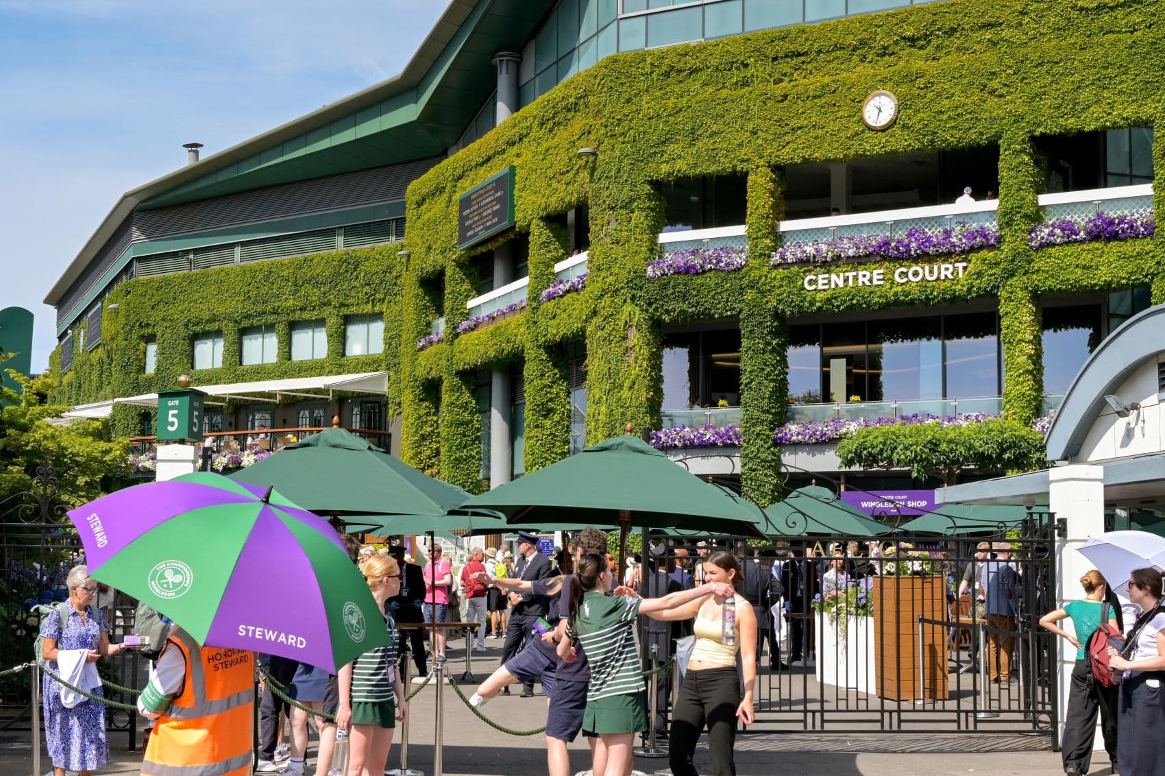 Außenansicht des Center Courts in Wimbledon, davor viele Besucher 