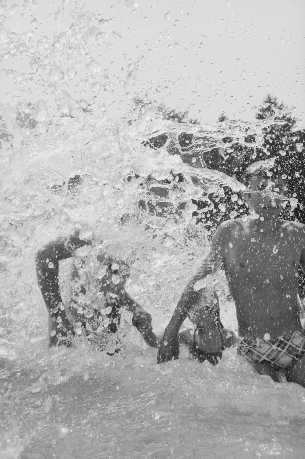 Schwarzweiss-Aufnahme: Badende tauchen unter einer Welle im Schwimmbad.
