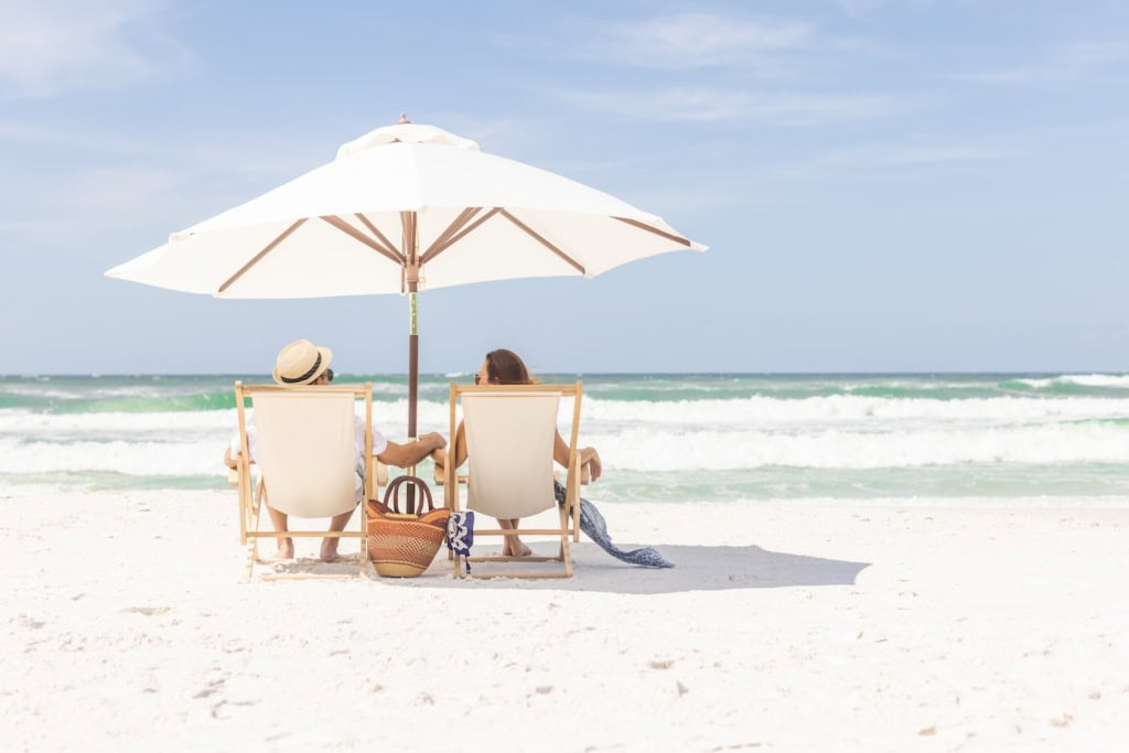 Händchenhaltendes Pärchen unter einem Sonnenschirm auf Liegestühlen am Strand von Florida
