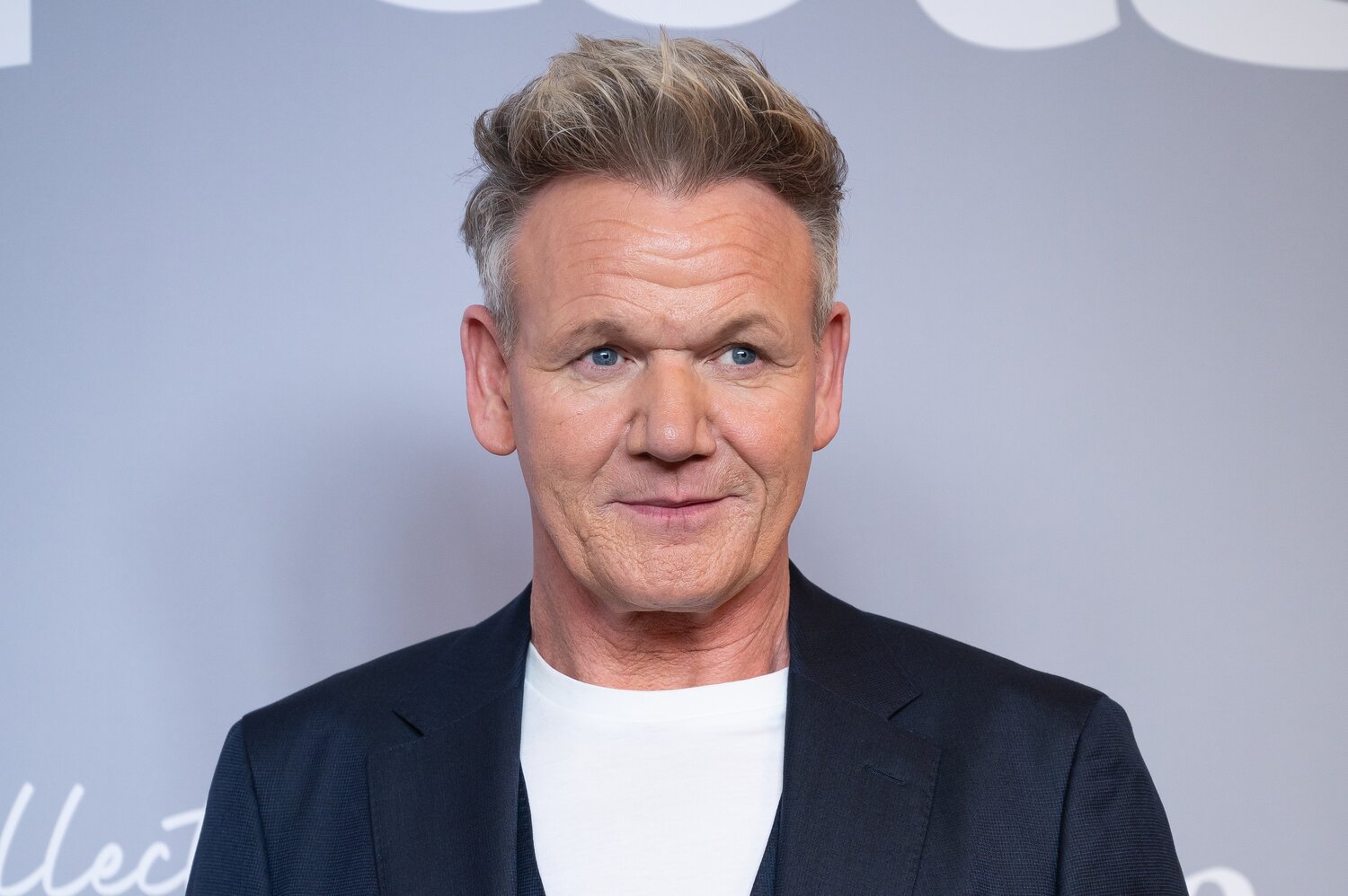 Porträt von Gordon Ramsay in dunklem Sakko über weißem T-Shirt vor hellgrauer Fotowand bei einem Presse-Termin.