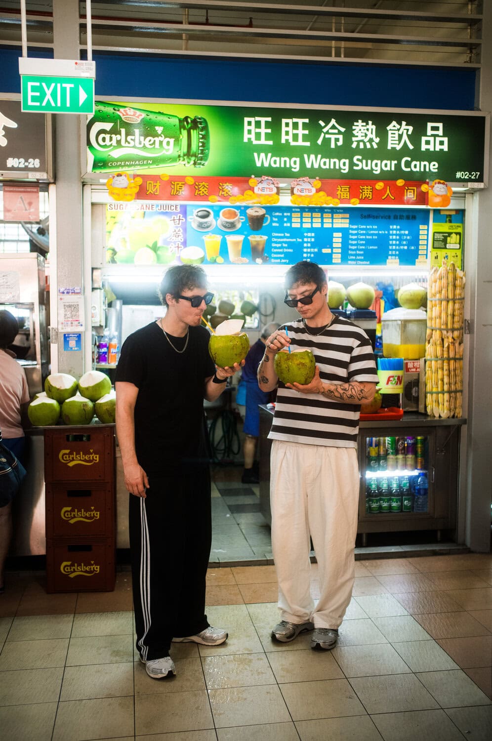 Heiko und Roman Lochmann trinken mit Sonnenbrillen frische Kokosnüsse vor einem Zuckerrohrsaft-Stand in einem Hawker Centre in Singapur.