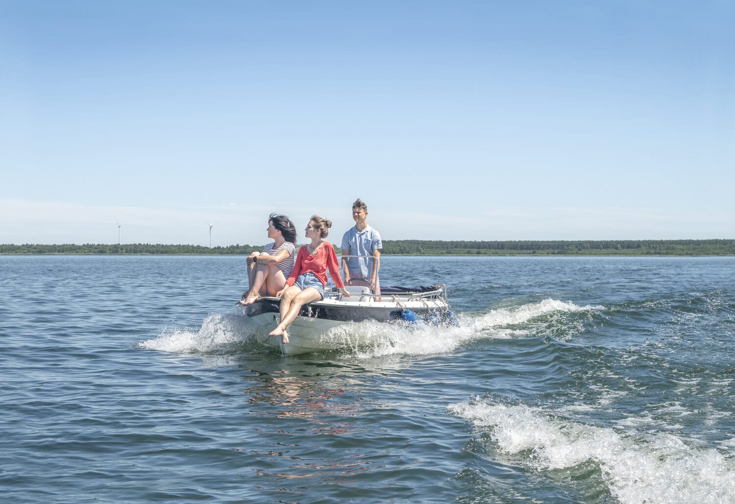 Drei Personen fahren bei Sonnenschein mit einem Motorboot ueber einen See im Lausitzer Seenland.