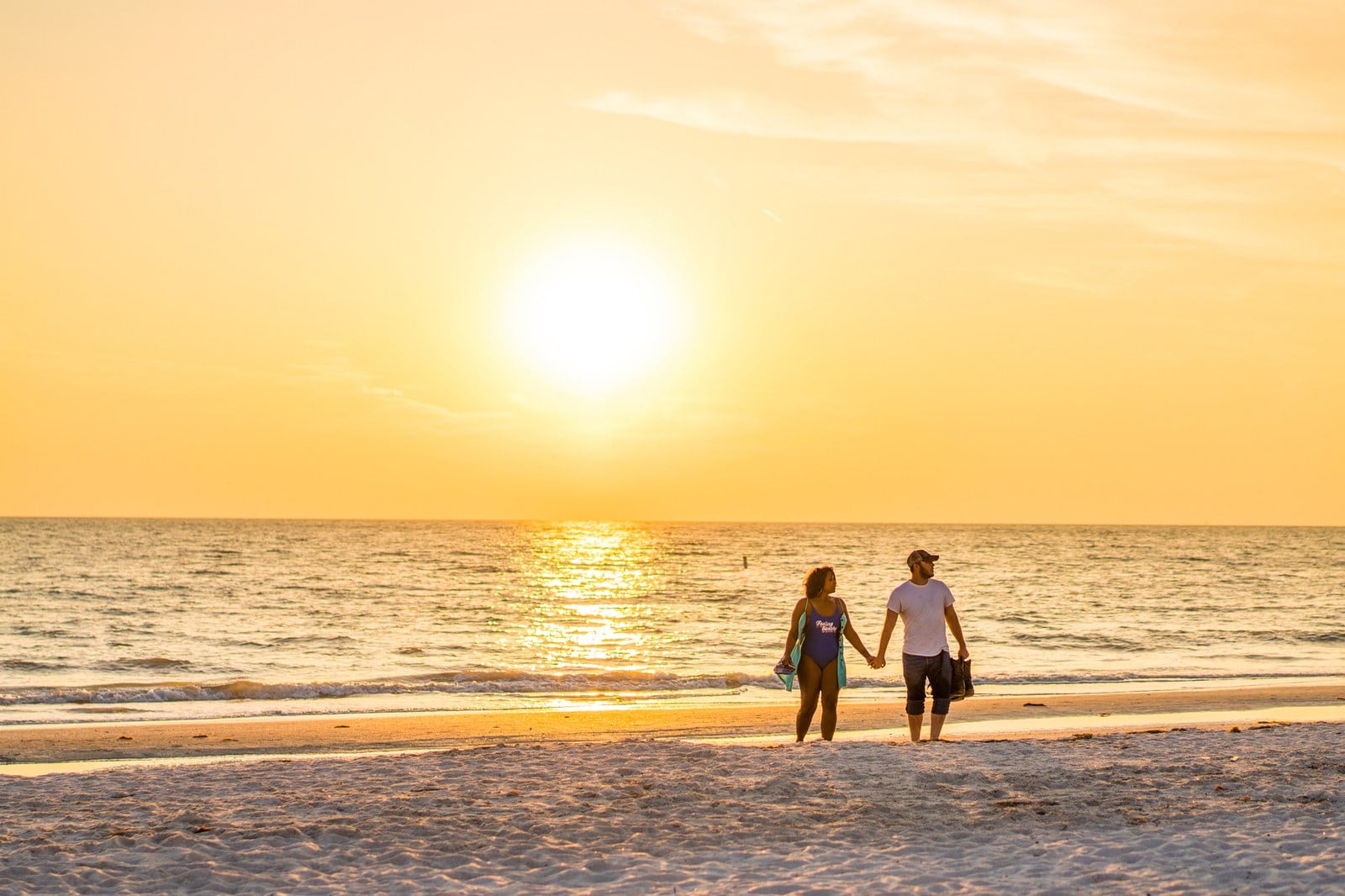 Paar geht Hand in Hand bei goldenem Sonnenuntergang am St. Pete Beach entlang des Wassers