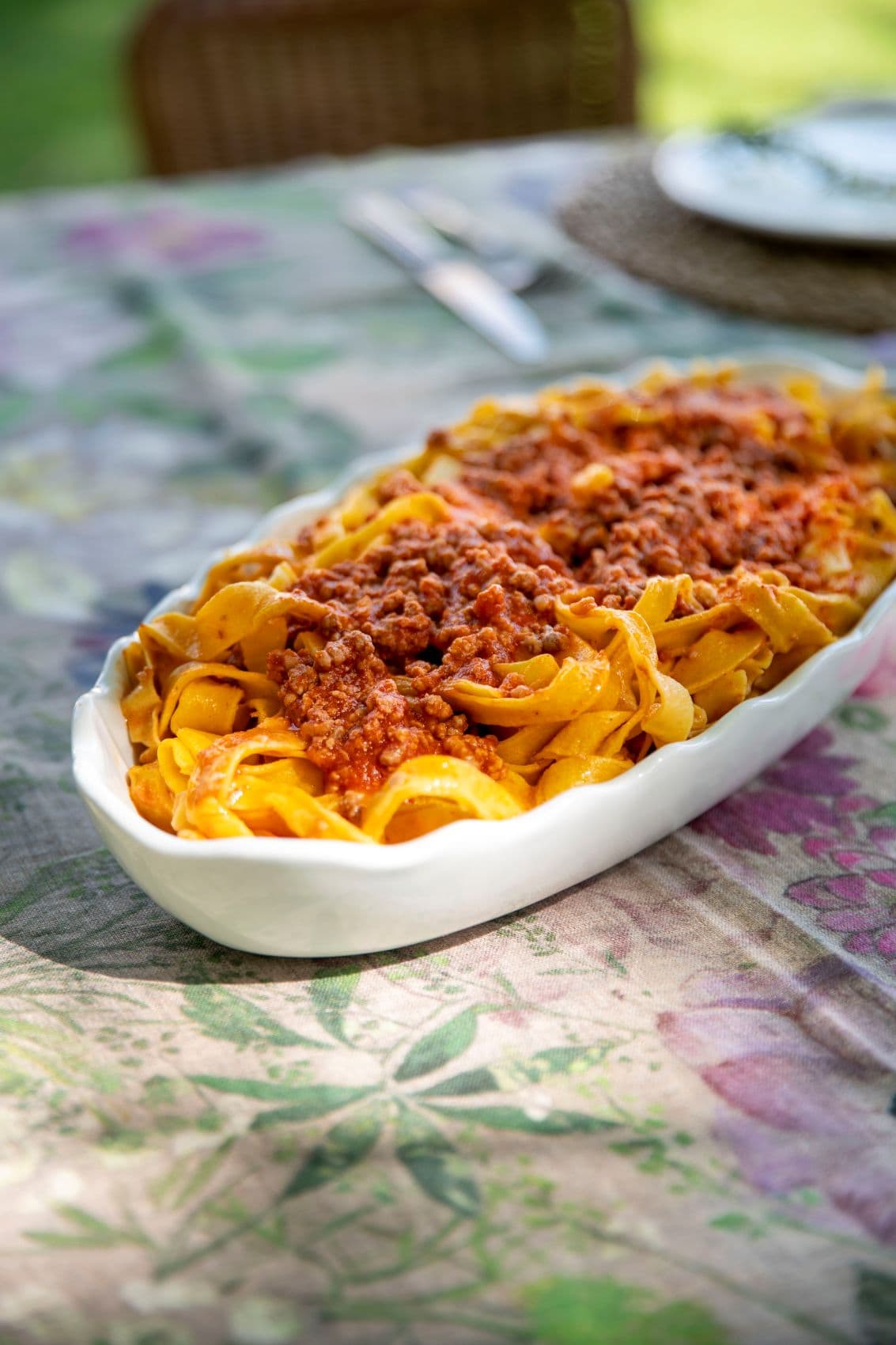 Tagliatelle al Ragù in einer weißen Servierschale auf einem gedeckten Tisch. Das traditionelle Pastagericht stammt aus der Emilia-Romagna.