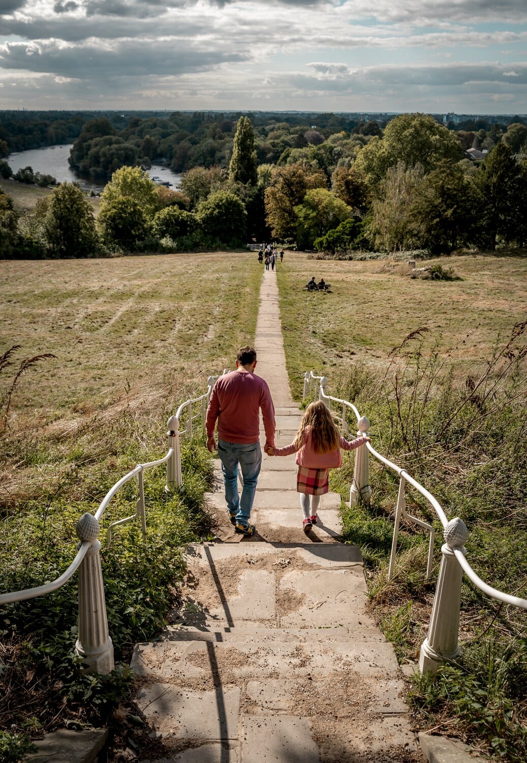 Vater und Tochter gehen Hand in Hand eine Treppe hinab mit Blick ueber die Themse bei Richmond Hill.