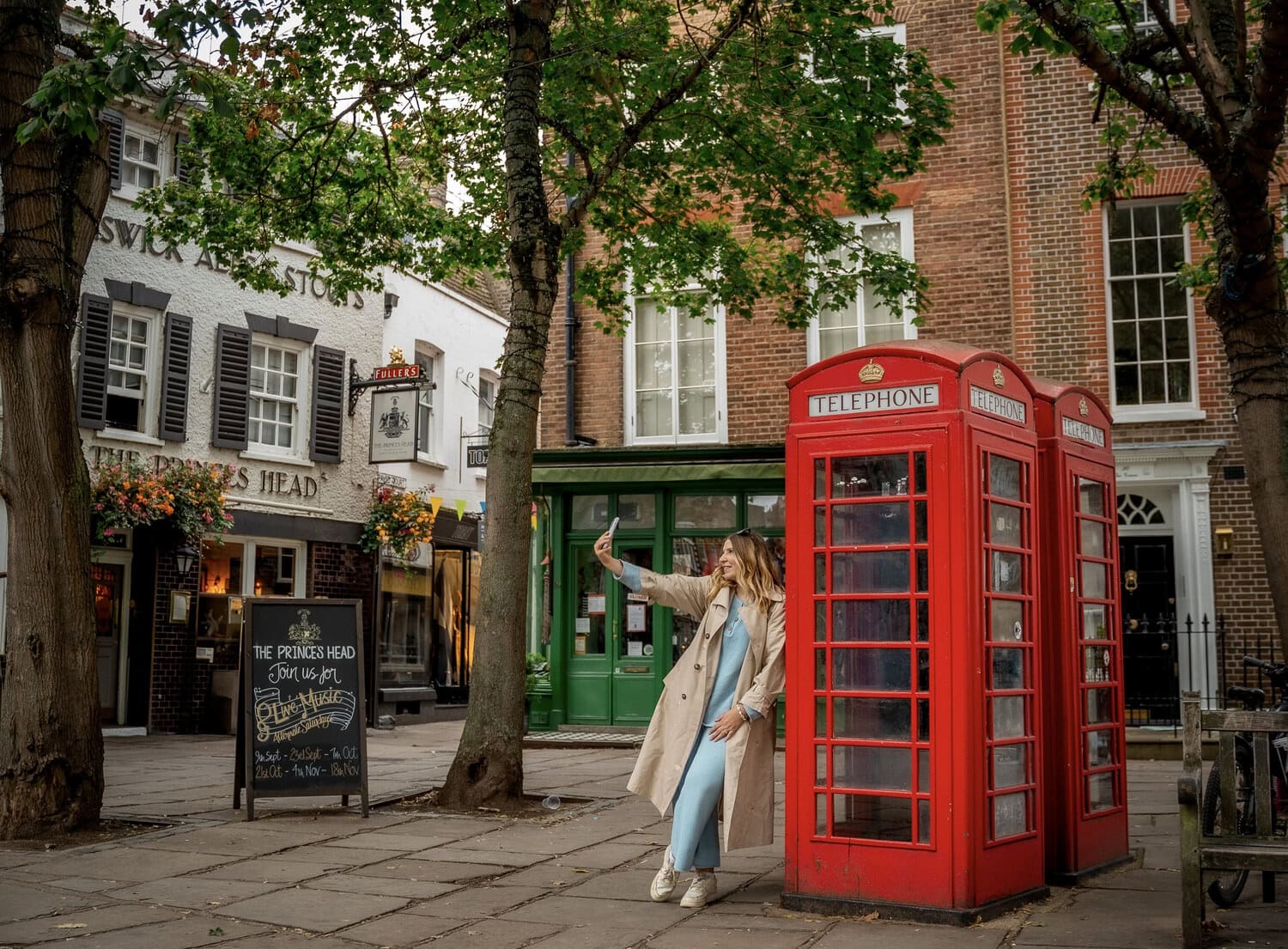Frau macht ein Selfie an zwei roten Telefonzellen vor einem traditionellen englischen Pub in Richmond.