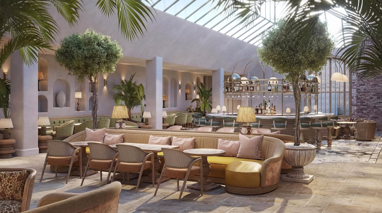 Lichtdurchflutete Orangerie-Lounge mit Glasdach, großen Olivenbäumen in Kübeln, geschwungenen Sofas in Rosé- und Grüntönen sowie einer Bar im Hintergrund.