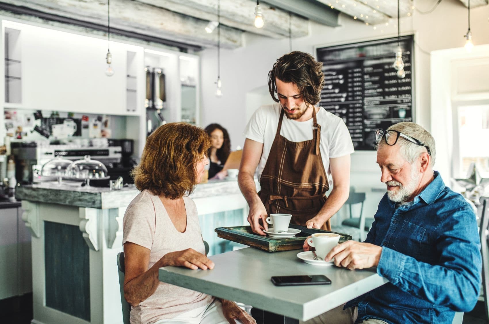 Mitarbeiter serviert einem älteren Paar Kaffee in einem Café