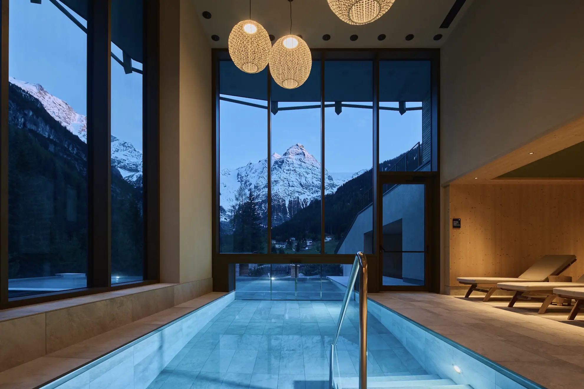 Innenpool im Wellnessbereich des Hotel Bella Vista Trafoi mit raumhohem Panoramafenster und Blick auf die verschneiten Gipfel des Nationalparks Stilfserjoch.