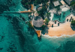 Luftaufnahme des Poolbereichs eines Luxusresorts bei Sansibar; das Meer rund um den Strandabschnitt ist türkisblau und klar.