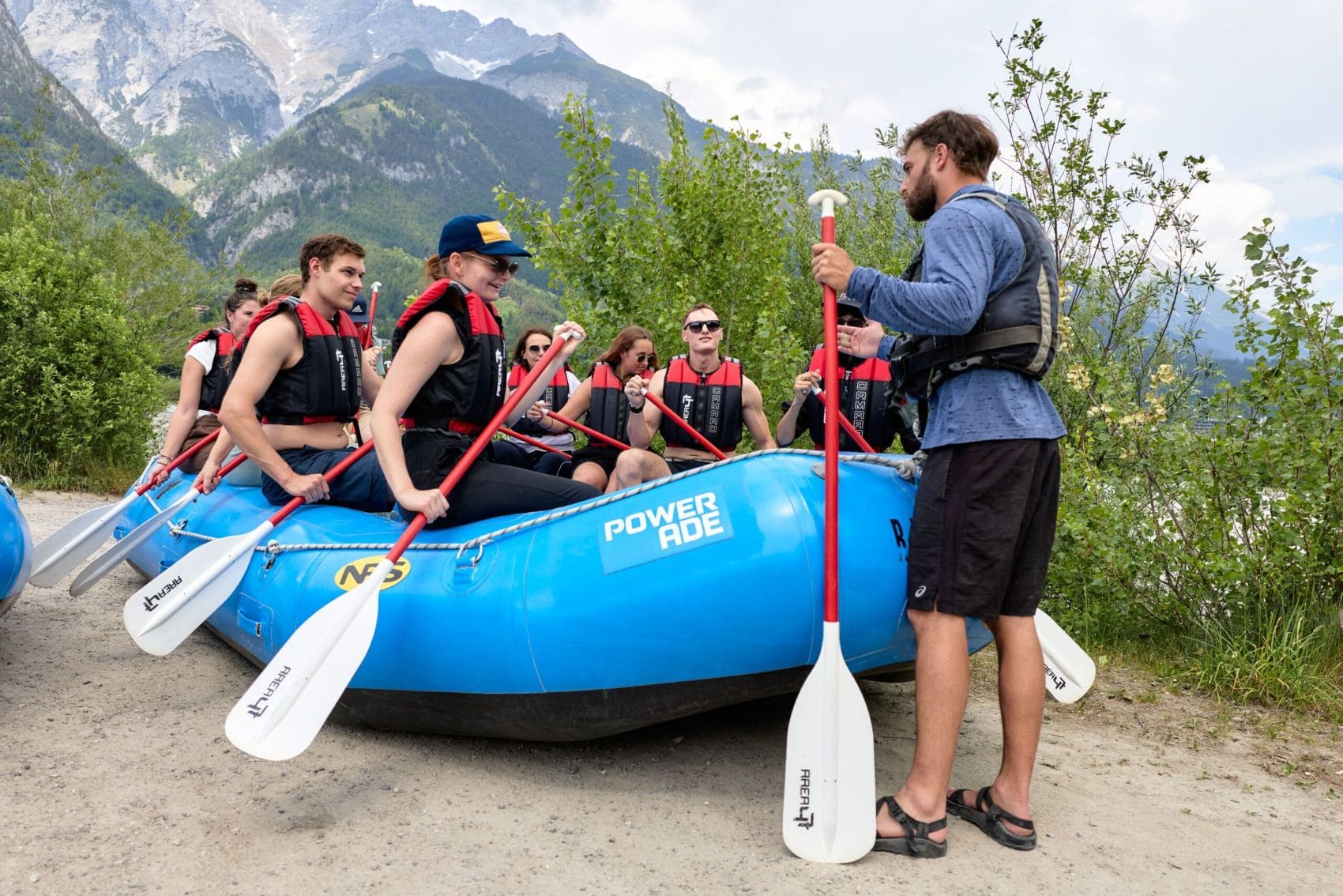 Teilnehmer erhalten vor einer Rafting-Tour bei Innsbruck eine Sicherheitseinweisung durch einen Guide vor der Alpenkulisse Tirols