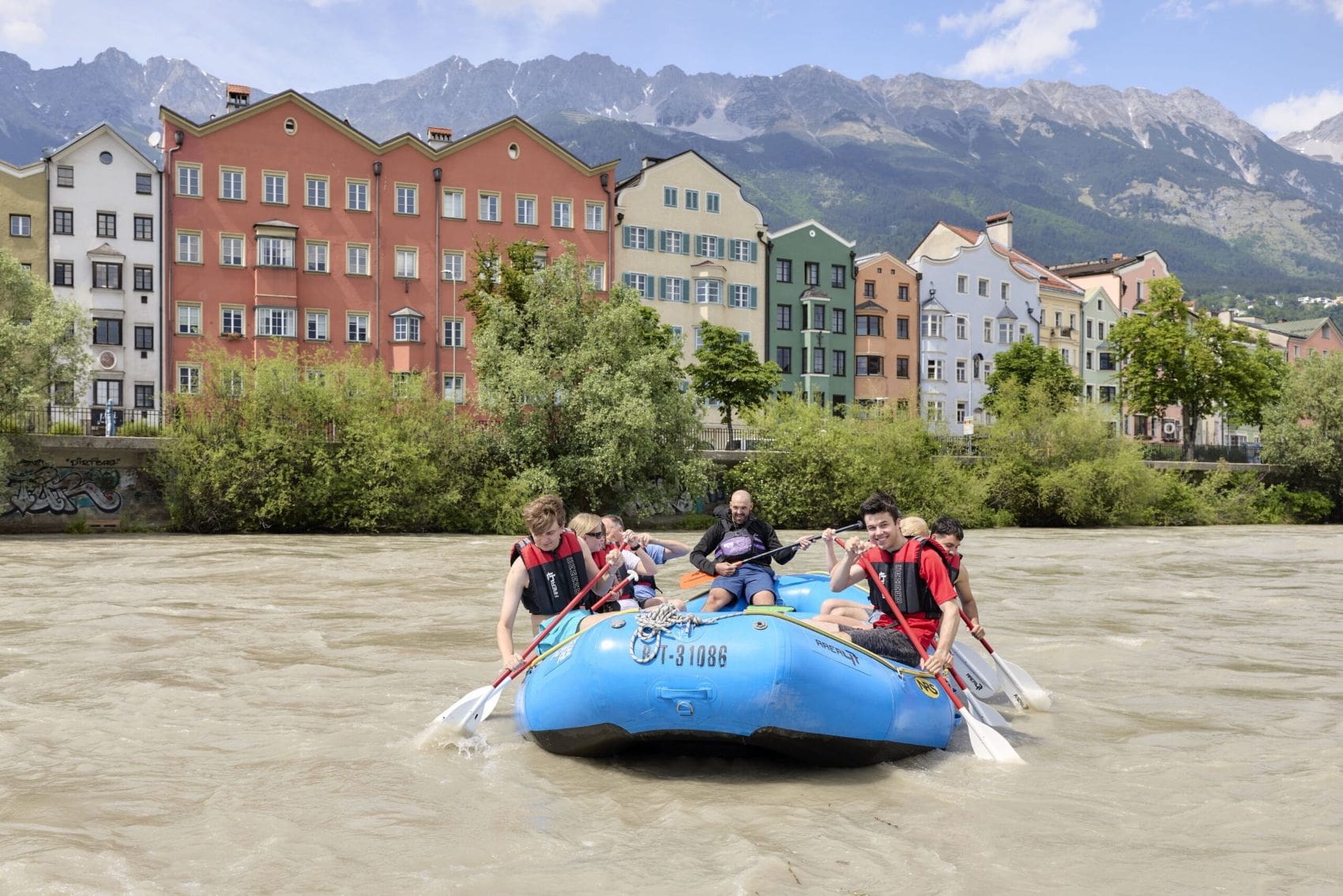 Teilnehmer einer Sightseeing-Rafting-Tour auf dem Inn vor den bunten Häusern Innsbrucks und der Nordkette in Tirol