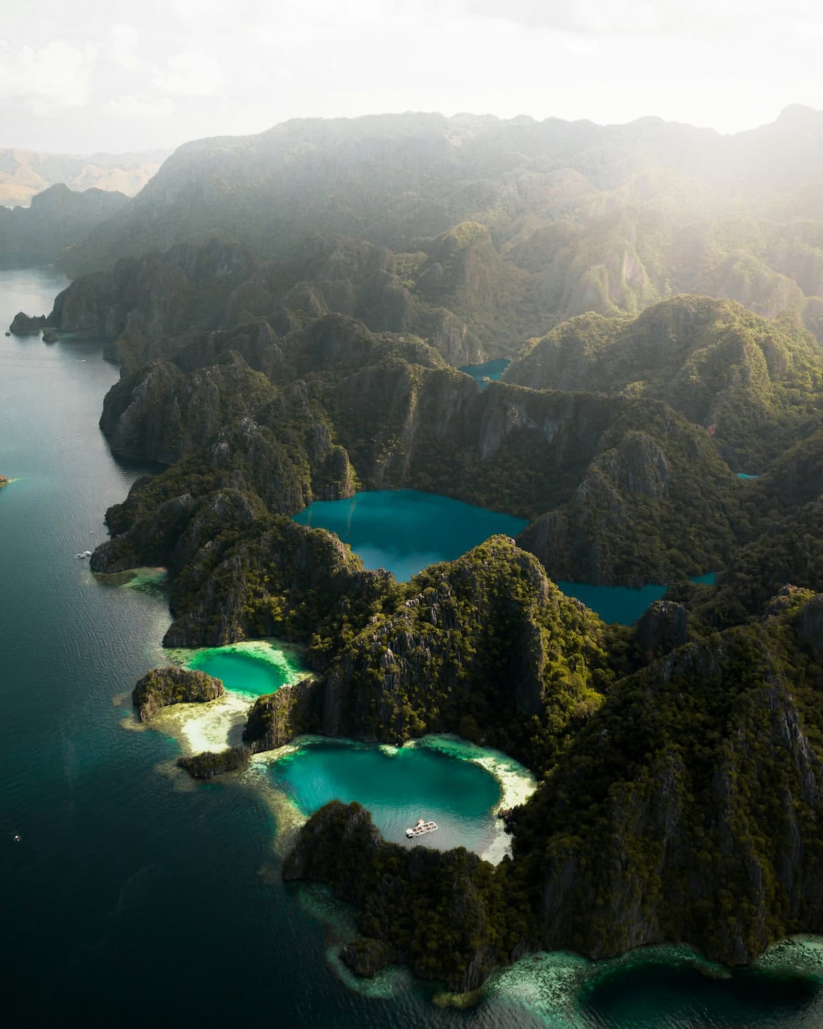 Karstfelsen mit dichtem Dschungel ragen aus dem Meer, dazwischen türkise und tiefblaue Lagunen, Luftaufnahme der Inselwelt von Coron auf den Philippine