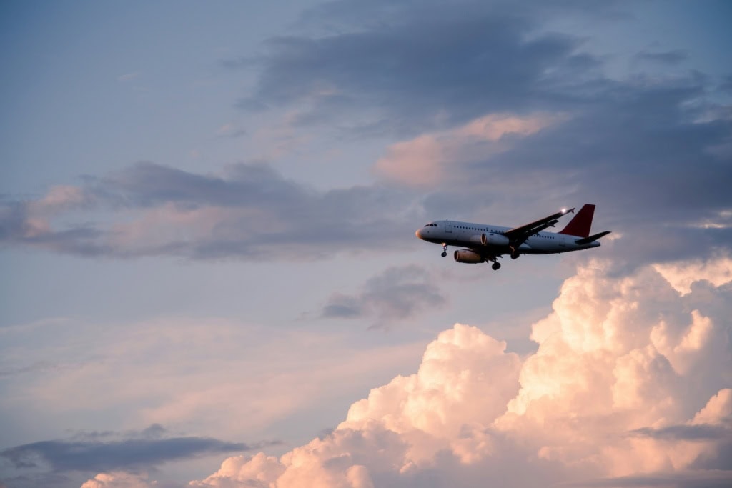 Analysierte Flugzeugbild und formulierte präzisen Alt-Text»Verkehrsflugzeug im Landeanflug mit ausgefahrenem Fahrwerk vor rosa beleuchteten Wolken im Abendhimmel.