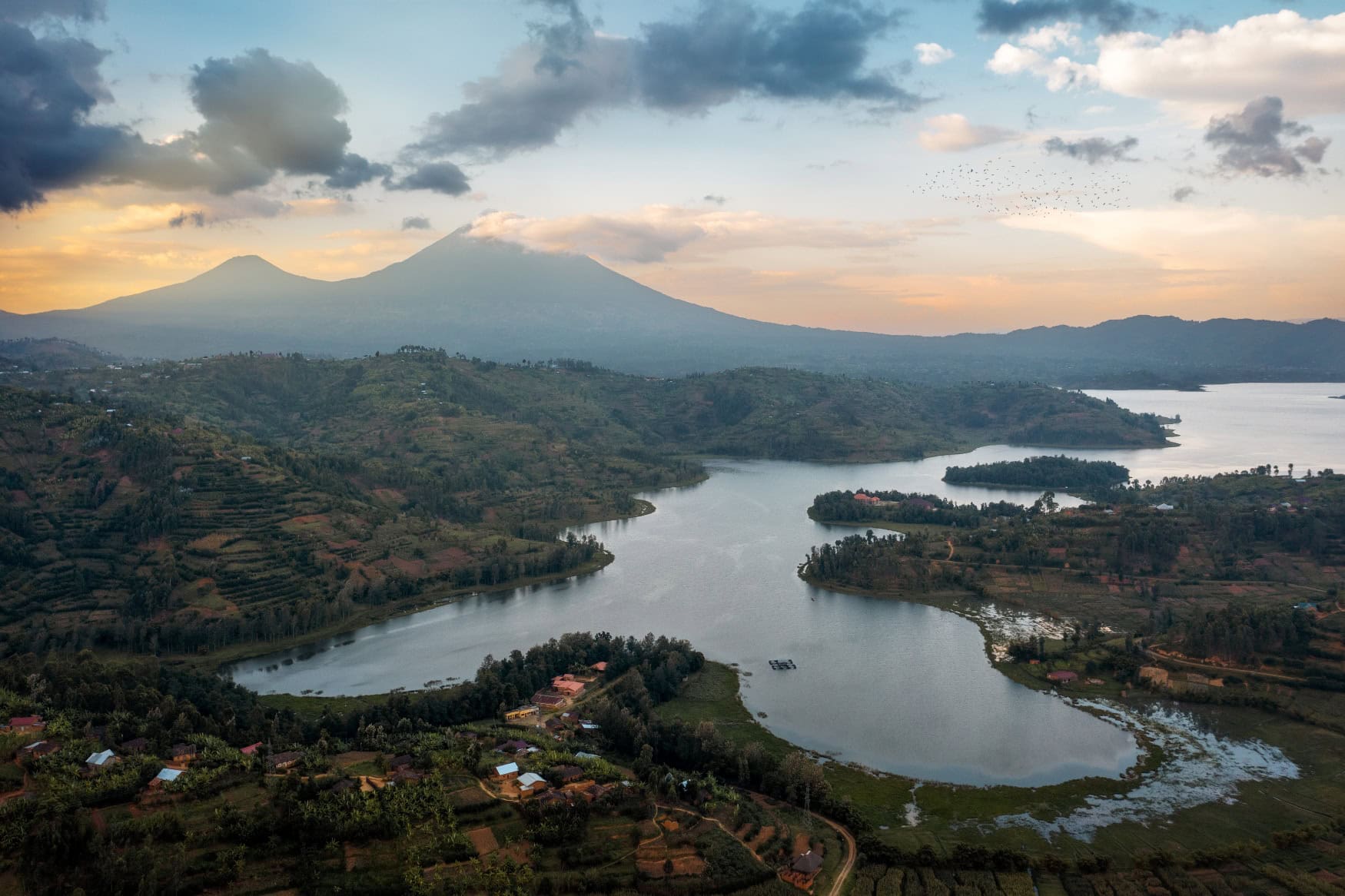 Blick auf eine Ebene mit einem großen See in Ruanda, am Horizont erhebt sich ein Gebirgszug mit dem Sabyinyo aus dem Dunst der Morgendämmerung.