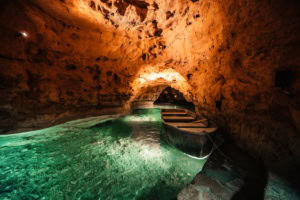 Ein kleines Boot liegt im türkisgrünen Wasser der Tapolca-Seehöhle, Ungarn – warm beleuchtete Felswände und ein Felstor im Hintergrund