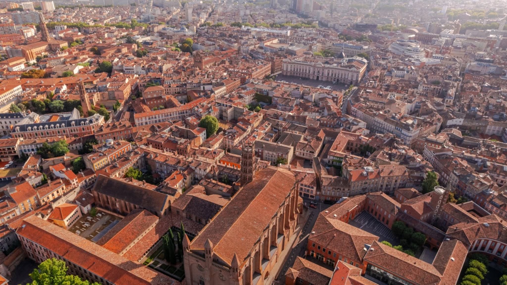 Drohnenaufnahme der Altstadt von Toulouse mit charakteristischen rosa-roten Backsteingebäuden und der Place du Capitole.