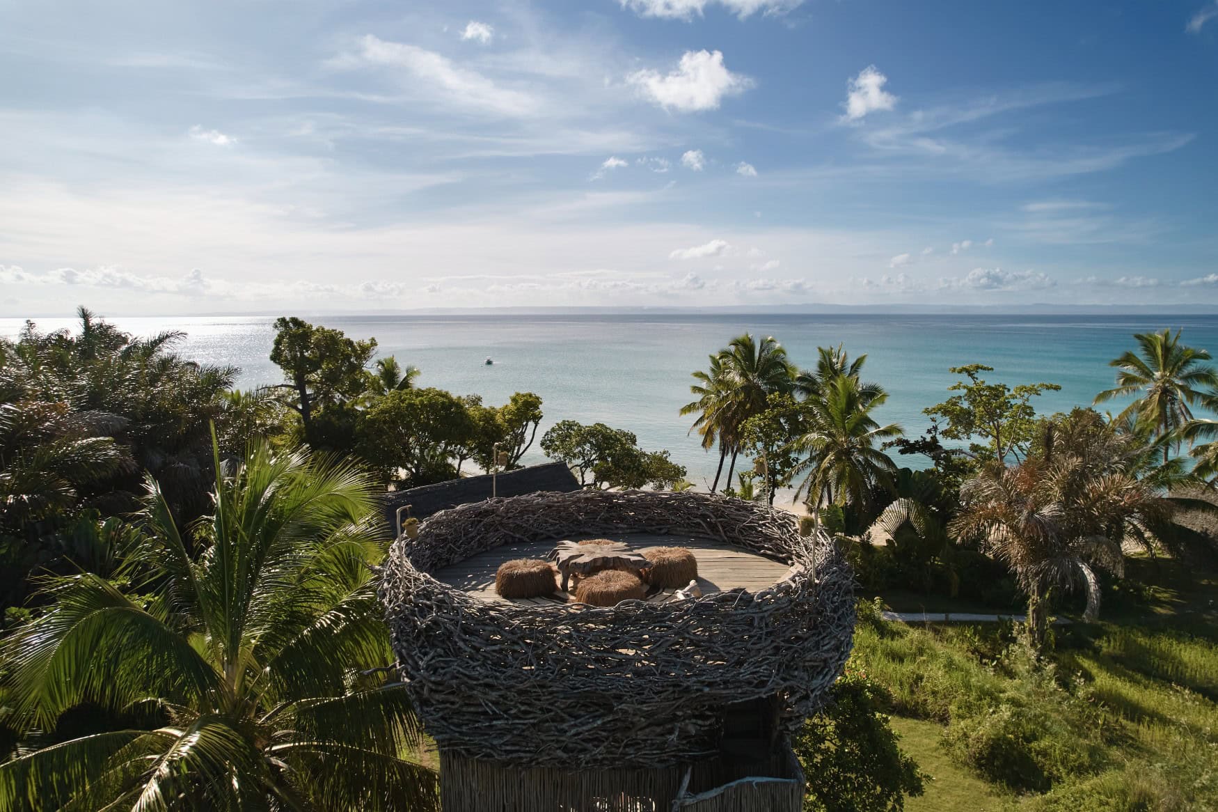 Das "Bird's Nest" des Voaara auf Madagaskar: eine runde Sitzplattform aus Treibholzgeflecht mit Blick über Palmen und tropische Vegetation auf das weite türkisblaue Meer.