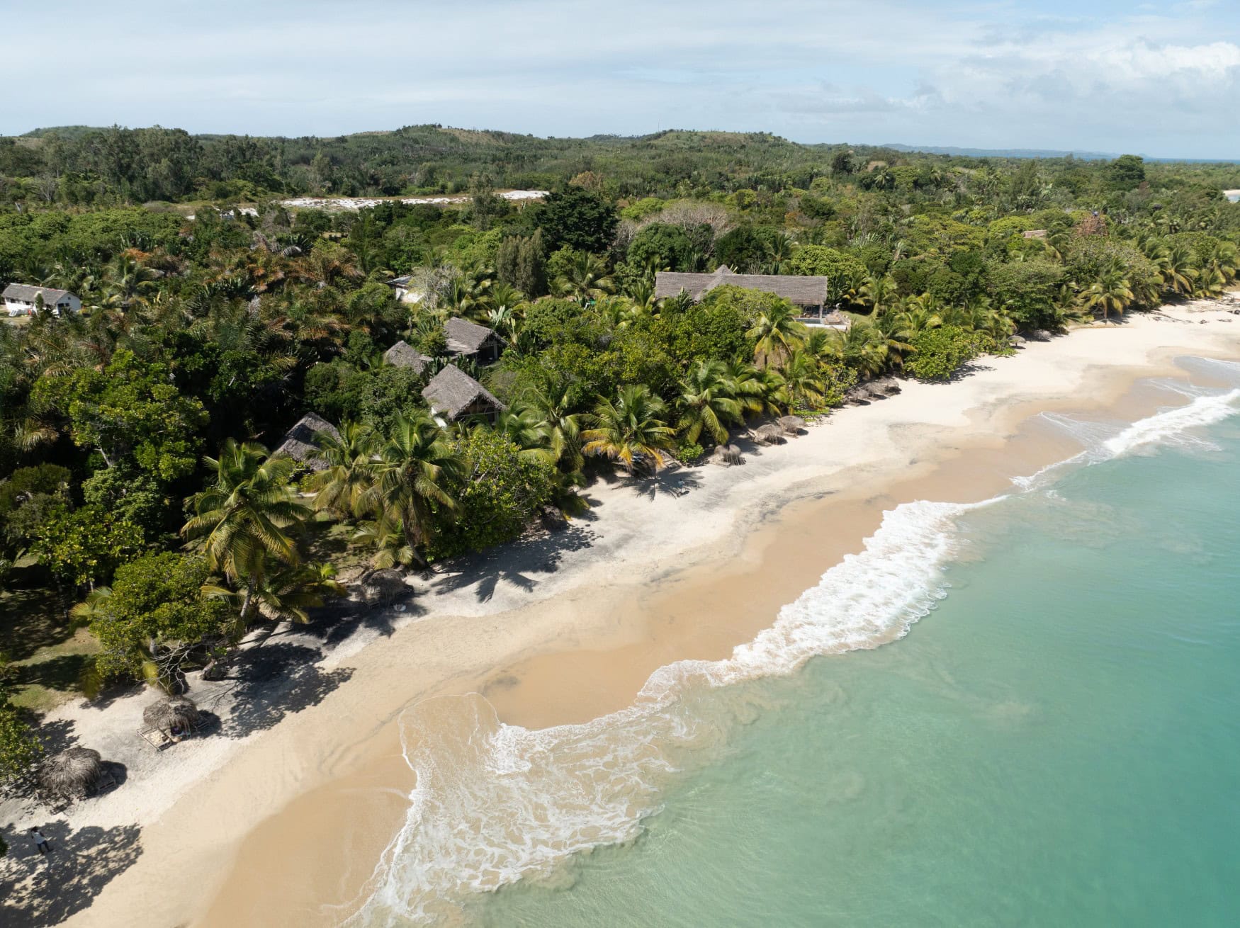Luftaufnahme der Voaara-Anlage auf Madagaskar mit Strohdach-Bungalows, die zwischen üppiger Tropenvegetation am langen weißen Sandstrand mit türkisem Meer liegen.