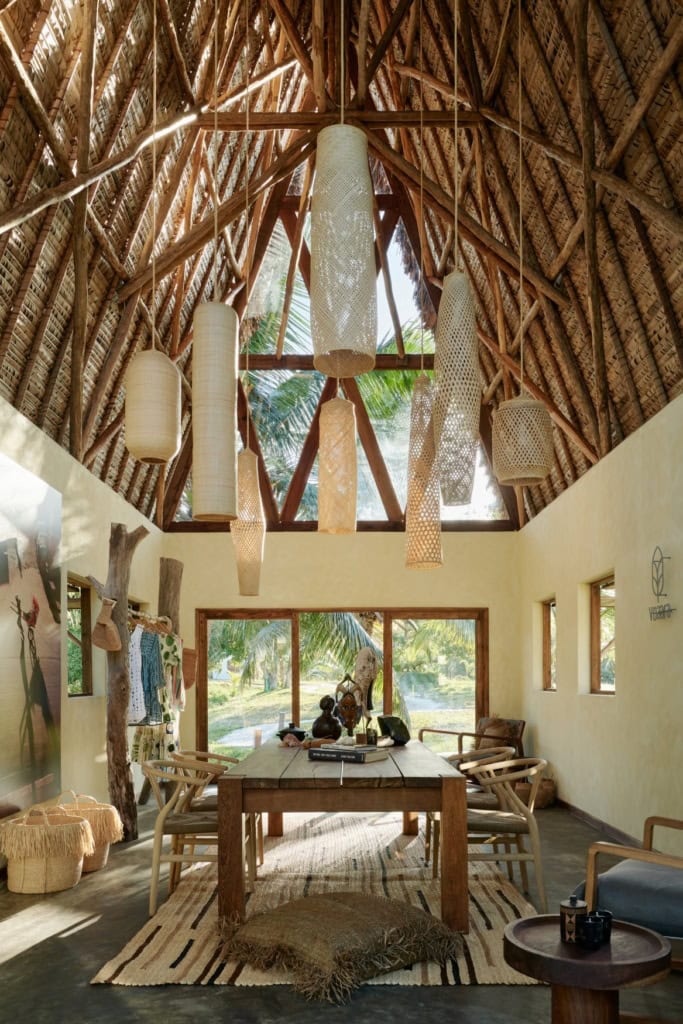 Innenraum der Villa des Voaara auf Madagaskar mit hohem Strohdach, mehreren hängenden Korblampen in verschiedenen Formen, einem langen Holzesstisch und dem Voaara-Logo an der Wand.